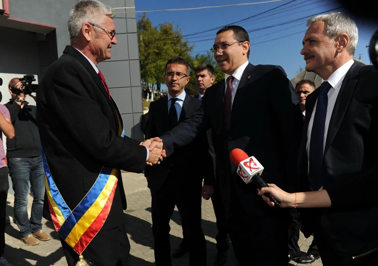 two men shaking hands in front of reporters