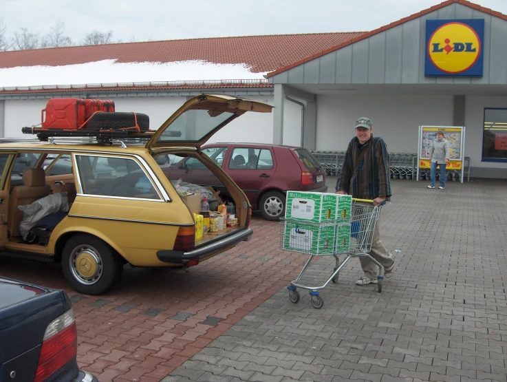 a man stands next to a car with its trunk open in a shopping mall
