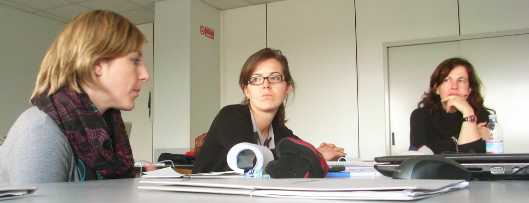 two women sitting at a table and one woman standing next to the other