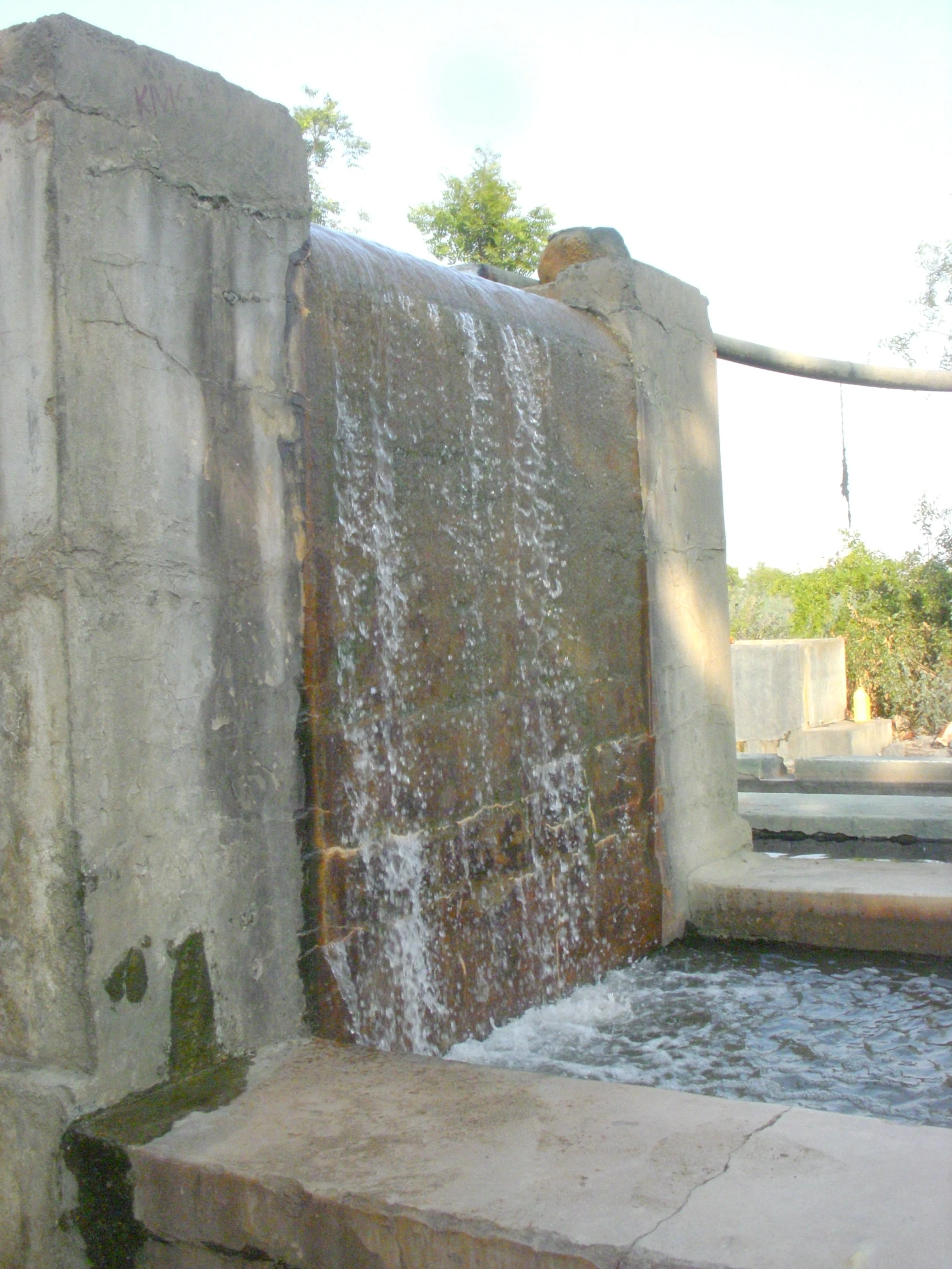 a waterfall with water falling from it next to a cement bench