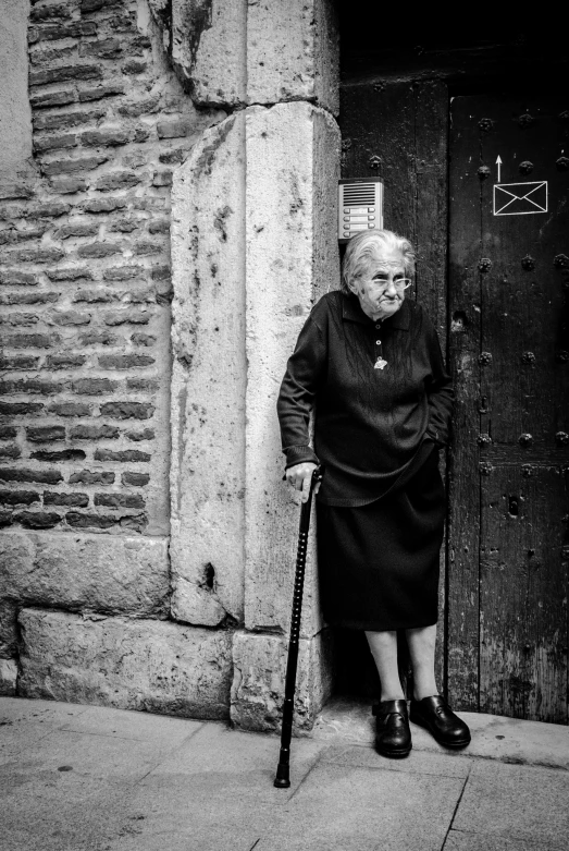 a woman leaning on the wall, holding a cane and looking in a door