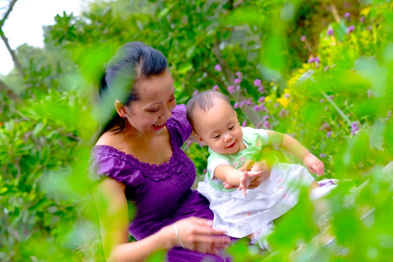 woman holding a baby in purple dress through trees