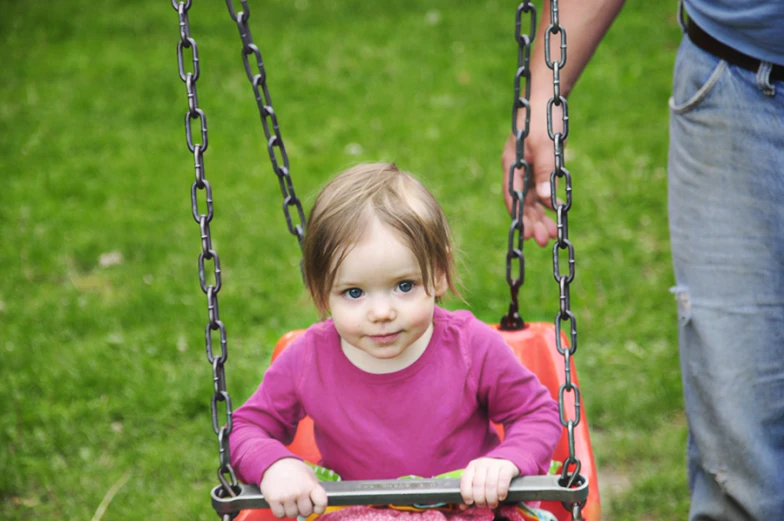 little girl sitting in swing while person holds on to chain