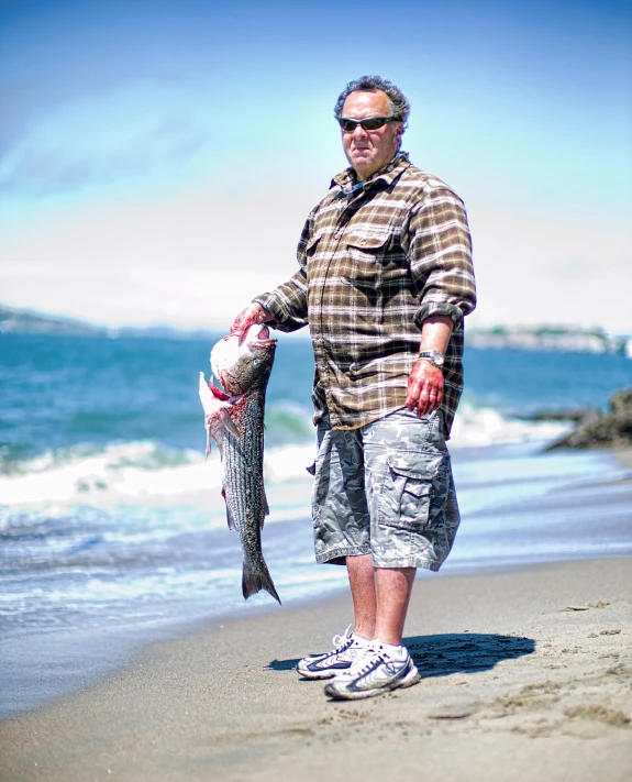 an old man with sunglasses and a fish is walking along the beach