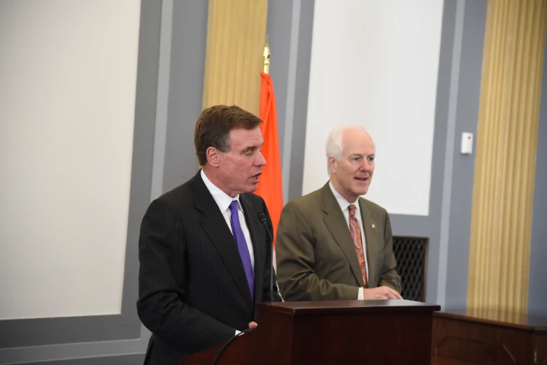 two men in suits stand at a podium