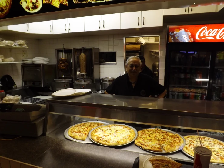 man working in a restaurant kitchen with three pizzas on the counter