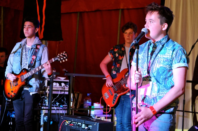 four men stand with guitar and microphone in front of an audience