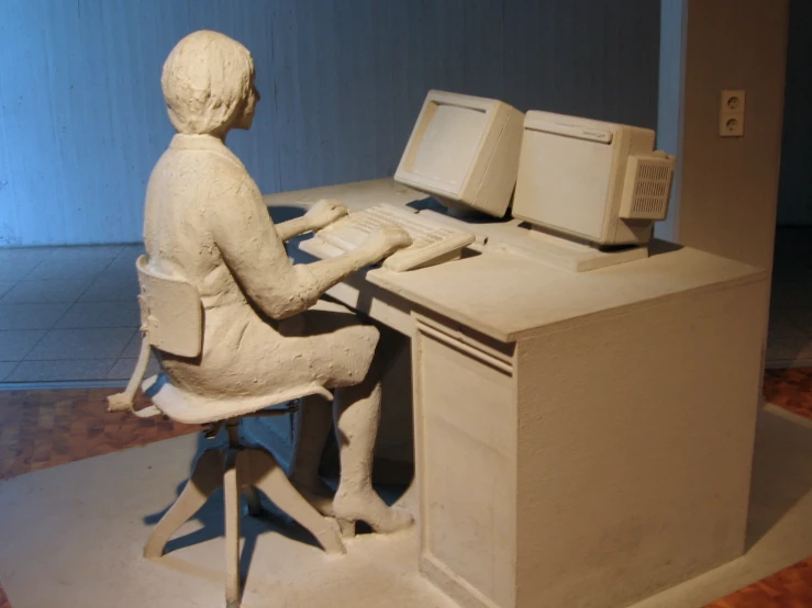 a statue of a woman sitting at a computer desk