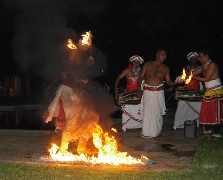 some people standing around a fire pit with torches in their hands