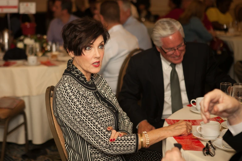 a woman points to someone as they sit at tables in a business setting