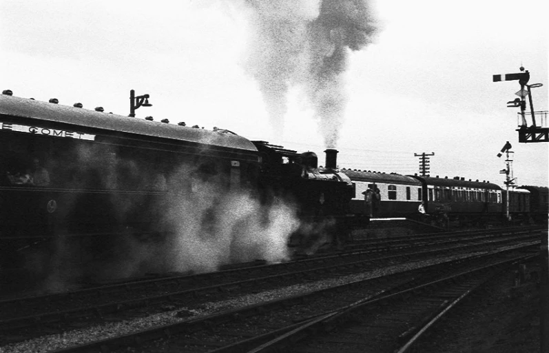 an old train emitting steam while standing on railroad tracks