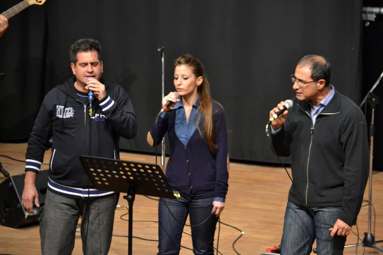 three people are singing and standing in front of a microphone