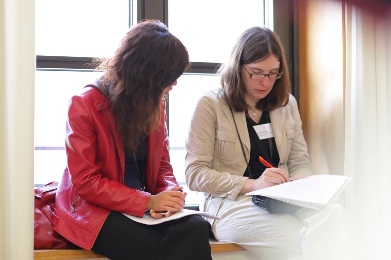 two women sitting together and working on soing