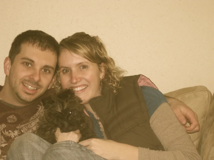 a couple is smiling on the couch while holding a dog