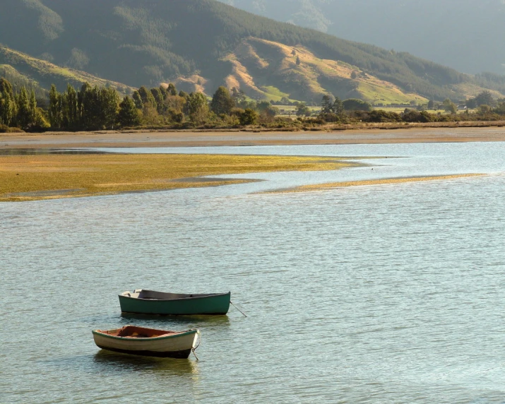 two small boats floating in the water near a mountain