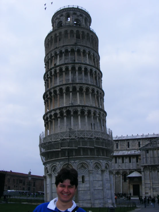 a smiling man poses for a picture in front of a leaning tower