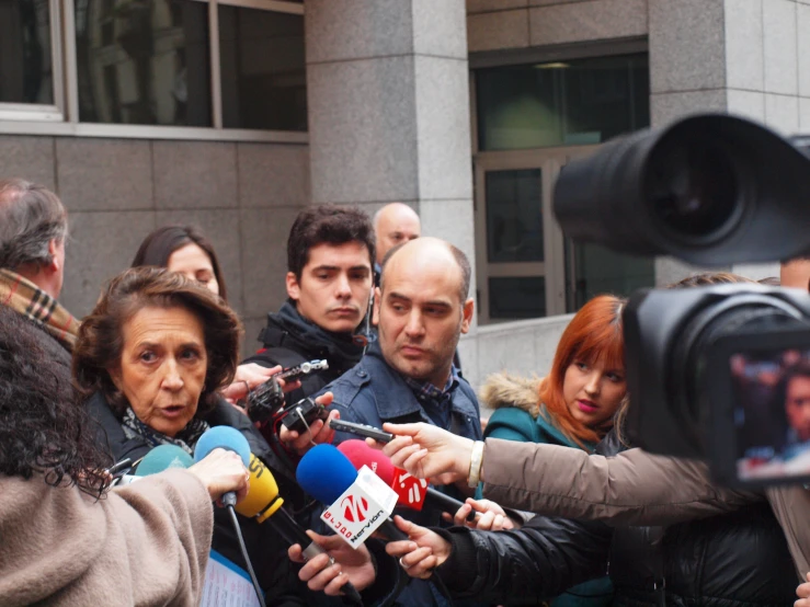 a man standing in front of microphones surrounded by media