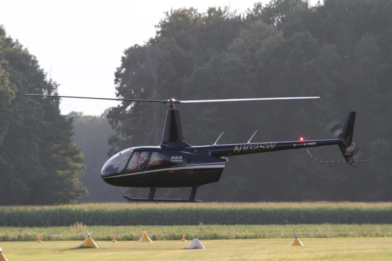 a black helicopter flying over the top of a field