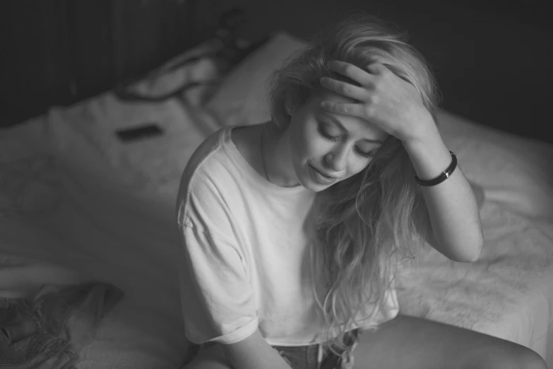 woman sits alone on a bed with her hands over her head