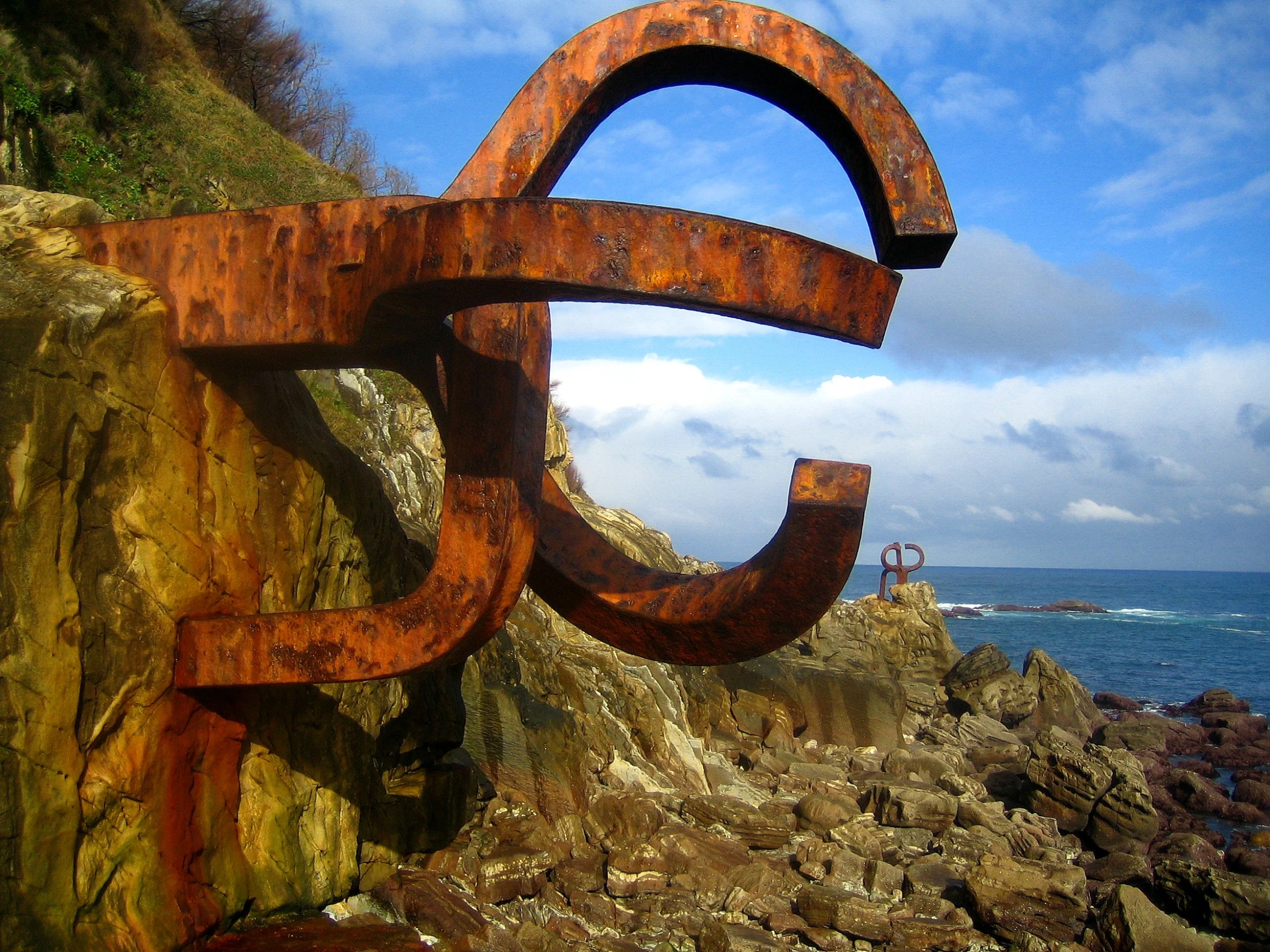 a rusty anchor sits on the rocks next to the ocean