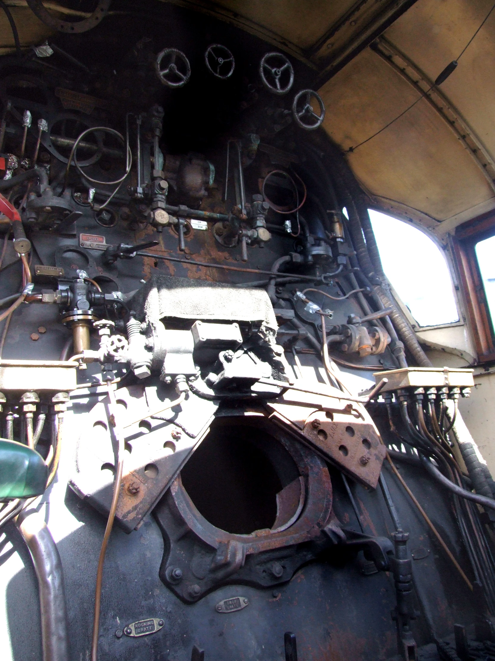 the engine of an old train with some pipes and gauges hanging from it