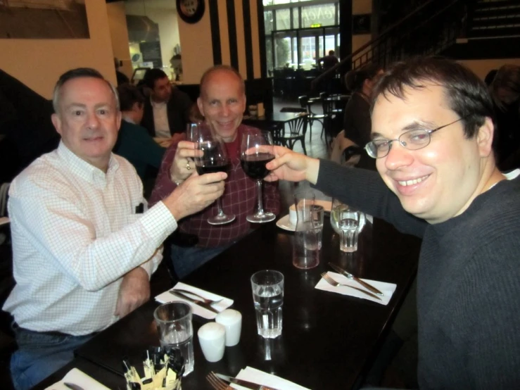 a group of men sitting down at a table and holding wine glasses