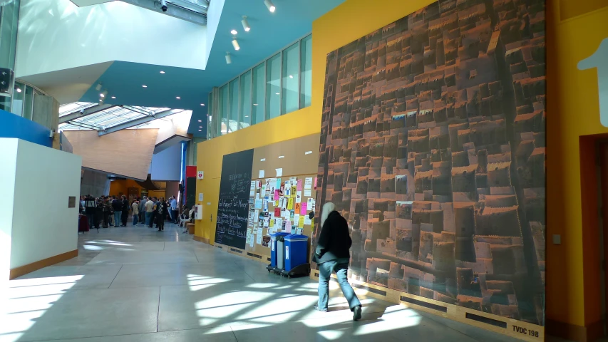 a man walks down a hall next to a wall with pictures on it