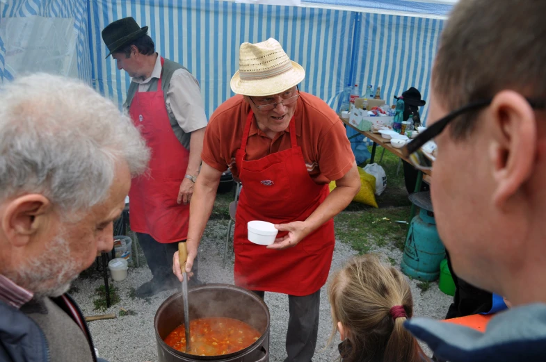 a man cooking soup with two women in red aprons