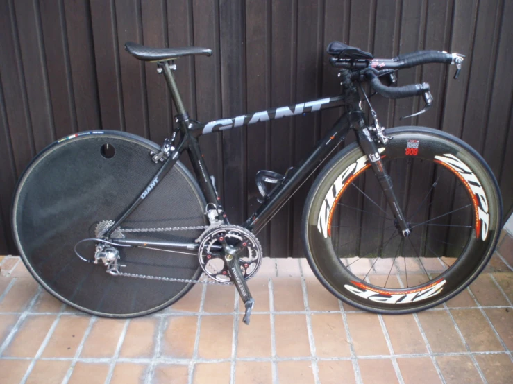 the black road bike with red and orange rims is parked by a wall