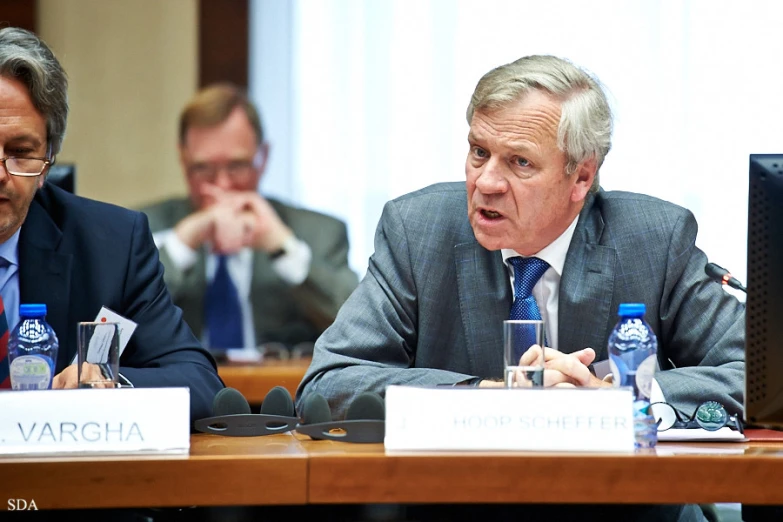 a man at a meeting sitting next to a table with another person