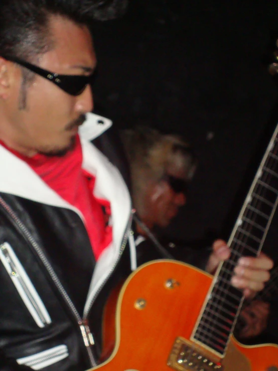 a man in a leather jacket and shades holding an orange guitar