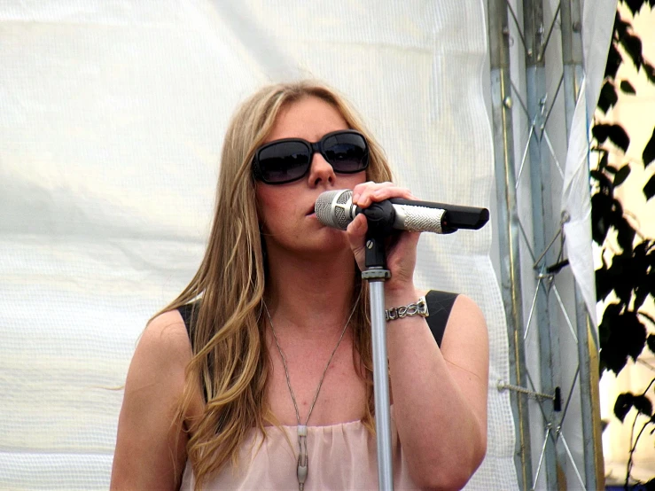 a woman wearing sunglasses singing into a microphone