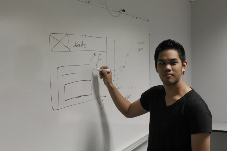 a young man pointing at a board with drawings on it