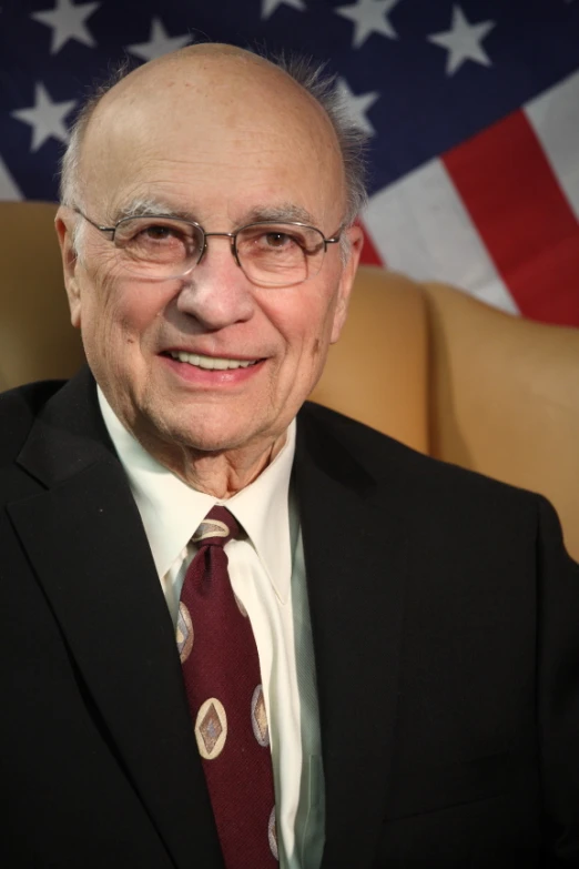 a smiling man with glasses and a maroon tie
