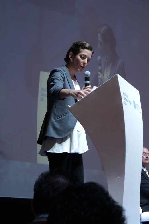 a woman in gray jacket speaking at podium