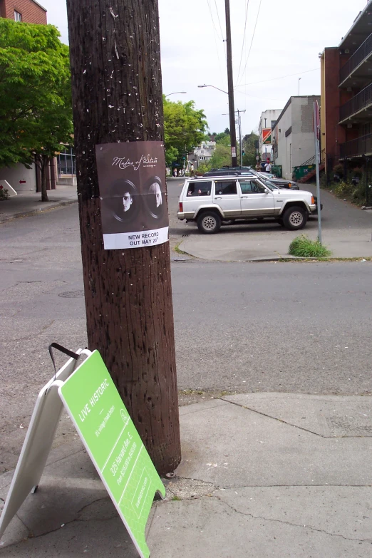 a broken sign posted on a telephone pole on a city street