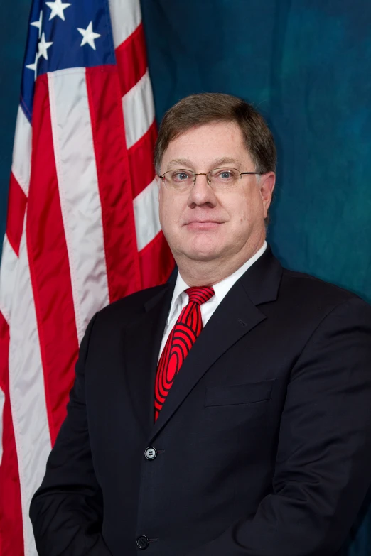 an official portrait of a man in front of an american flag