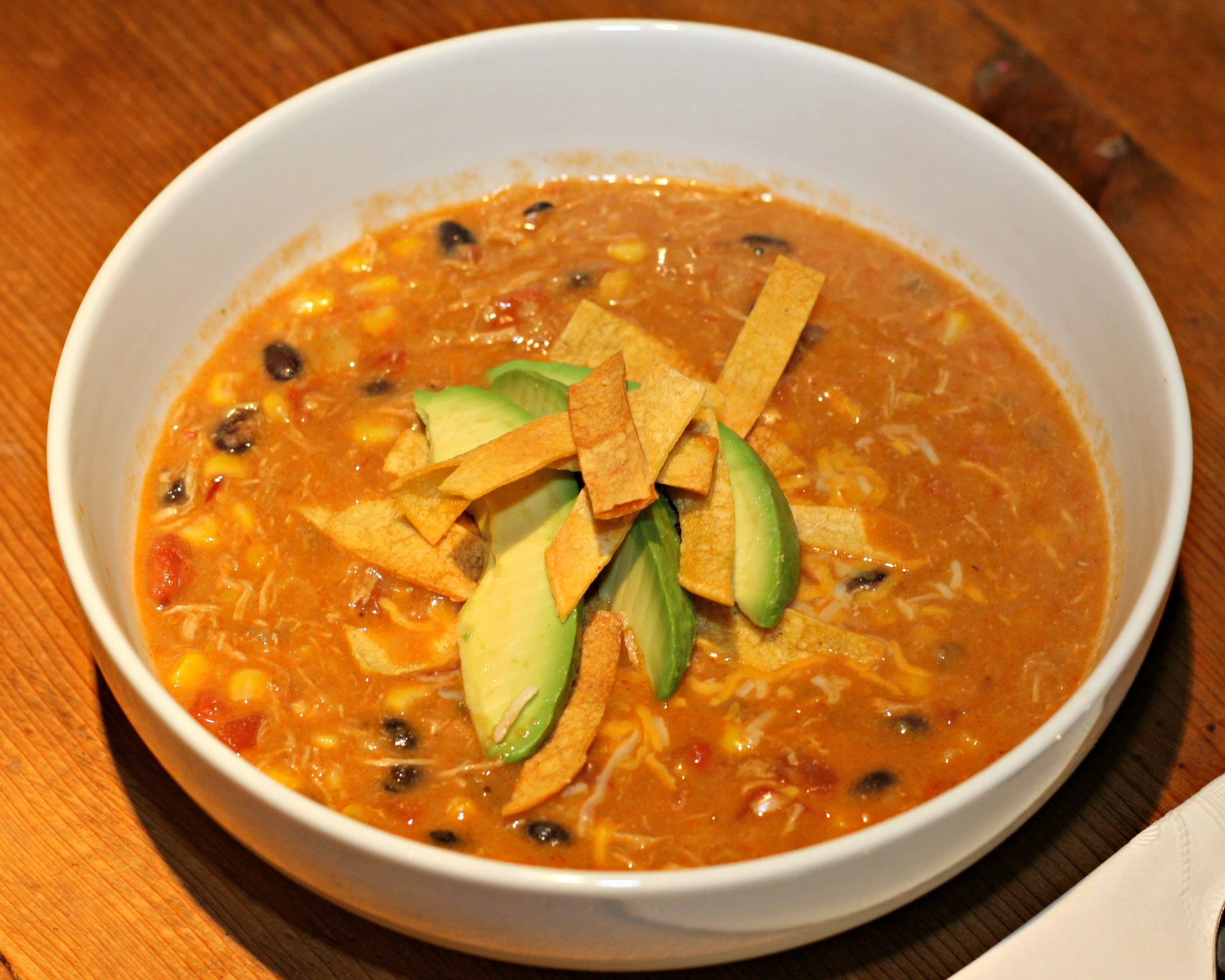 a bowl of soup with tortilla chips, avocado and cheese