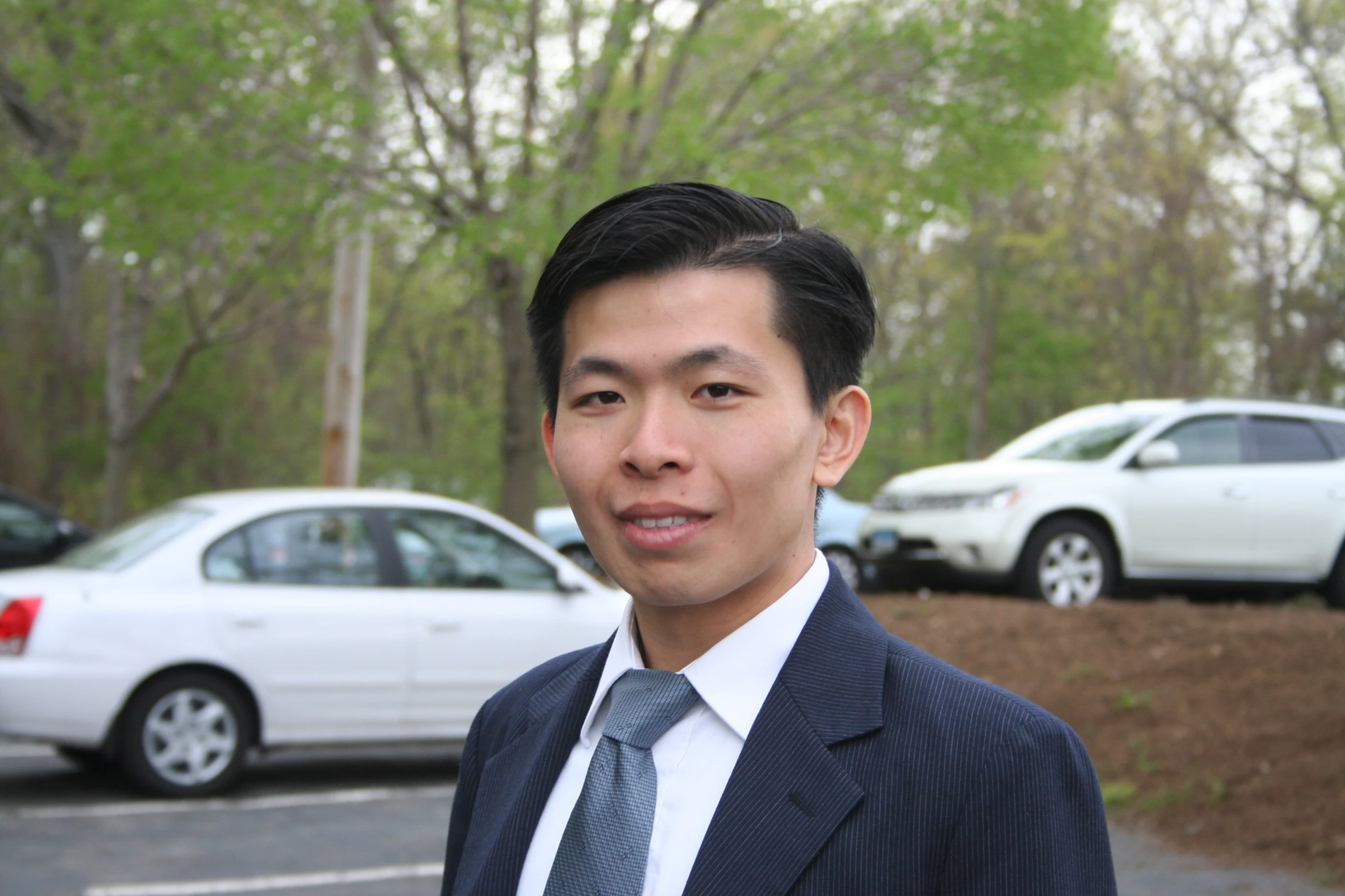 a man in suit and tie standing by cars