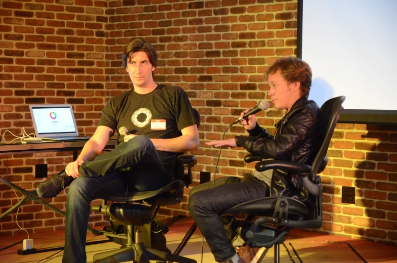 two people sitting at desks while holding microphones