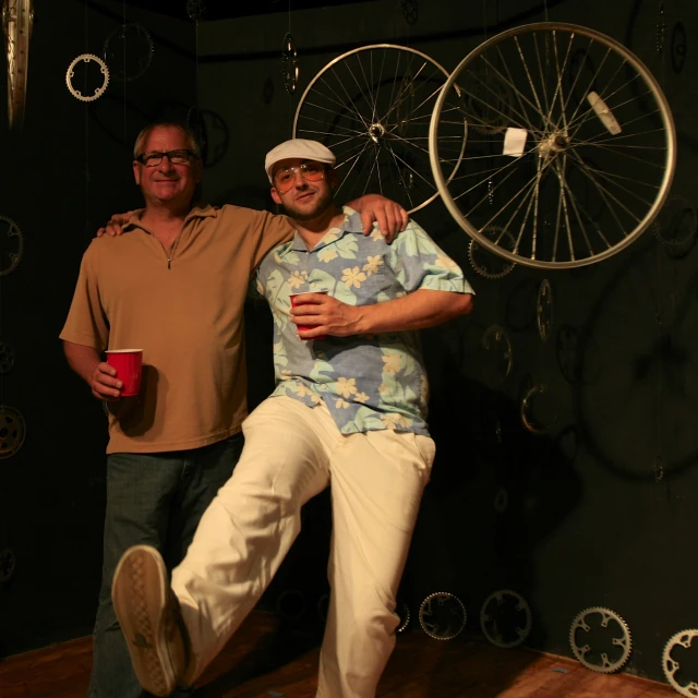 two men stand in front of an old - fashioned bike wheel sculpture