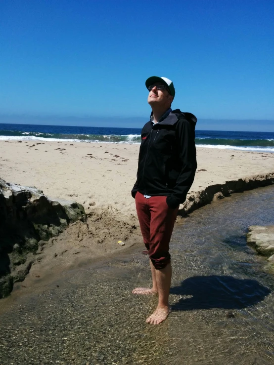 a man in red pants and black jacket stands on a beach