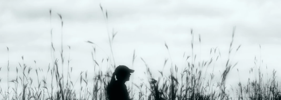 a black and white image of a silhouette of someone in the middle of some tall grass