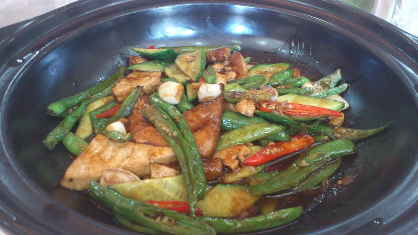 a black bowl with green and red peppers and meat