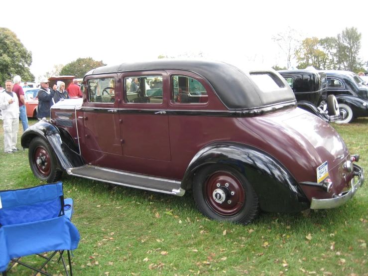 antique car sitting on the grass with others looking at it