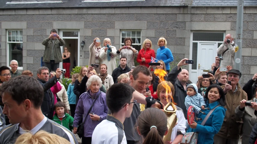 a crowd is gathered around an older man that is blowing fire out of a cigarette