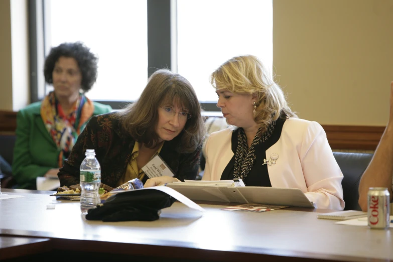 two woman are sitting at a desk with books