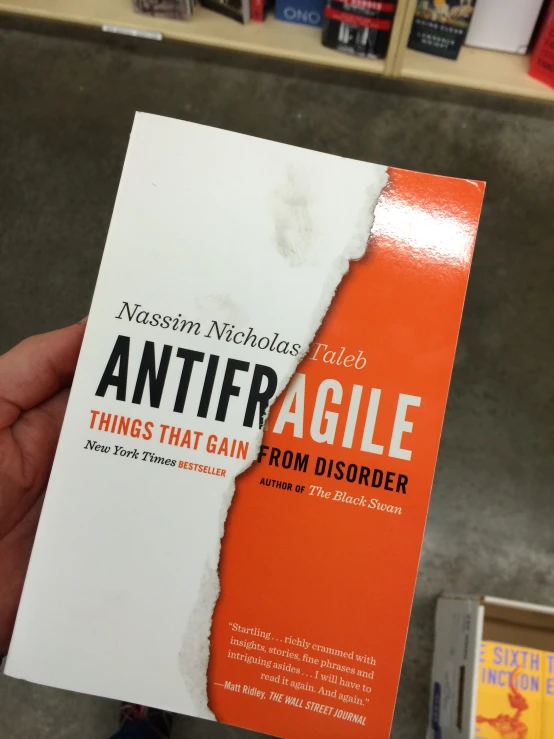 a hand holding a white and orange book with torn paper on the cover