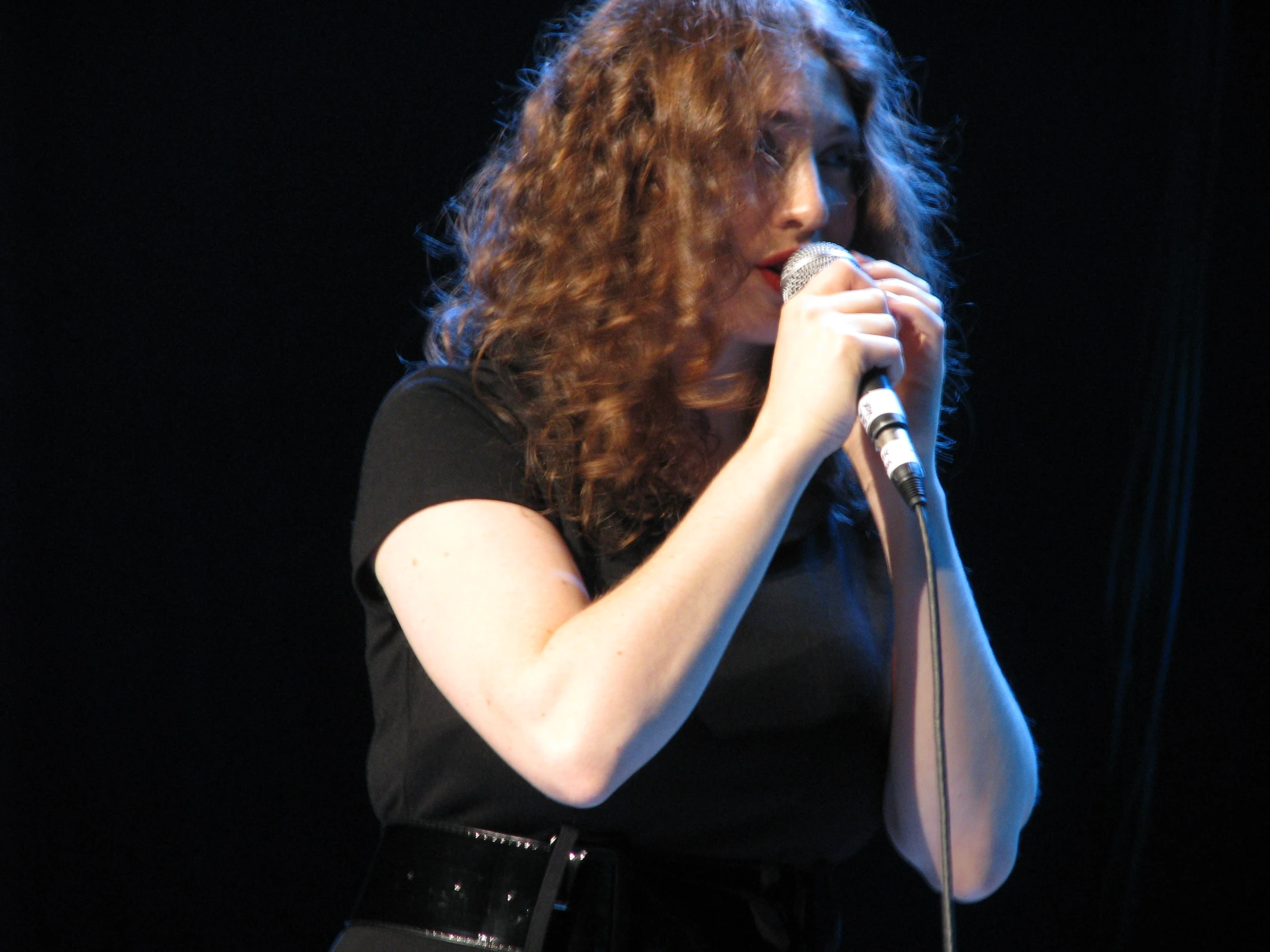 a woman in black shirt singing with microphone