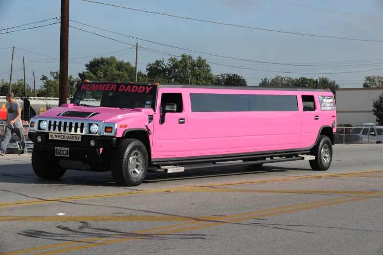 a pink limousine with a sign on the back driving down a street